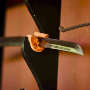 Tip view of a Katana blade resting on a black holder mounted on an orange wall
